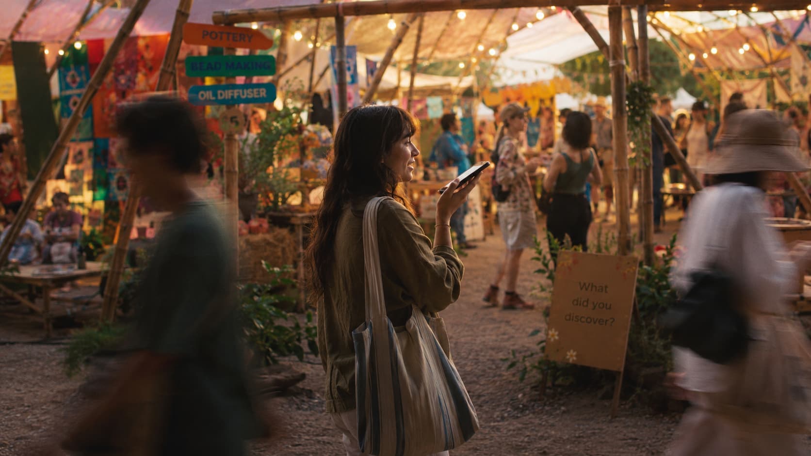 A woman speaking into her phone beside a “What did you discover?” sign at a market